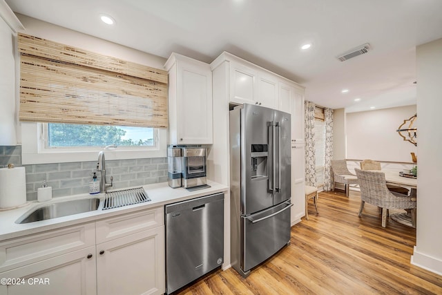 kitchen featuring sink, appliances with stainless steel finishes, white cabinets, decorative backsplash, and light wood-type flooring