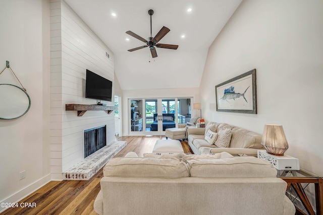 living room with light hardwood / wood-style flooring, high vaulted ceiling, a large fireplace, ceiling fan, and french doors