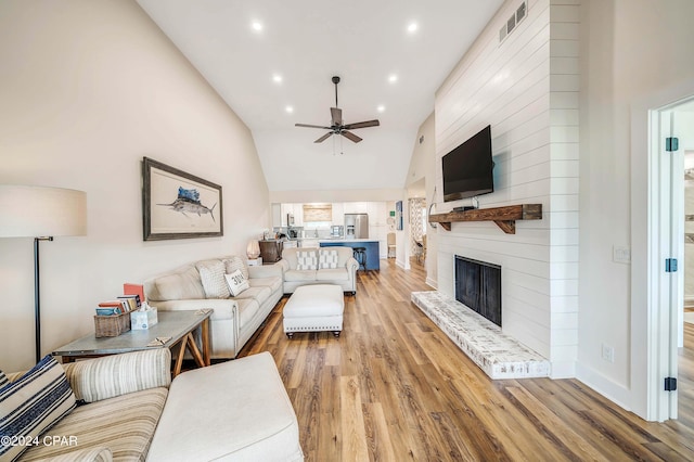 living room featuring vaulted ceiling, a large fireplace, ceiling fan, and light wood-type flooring