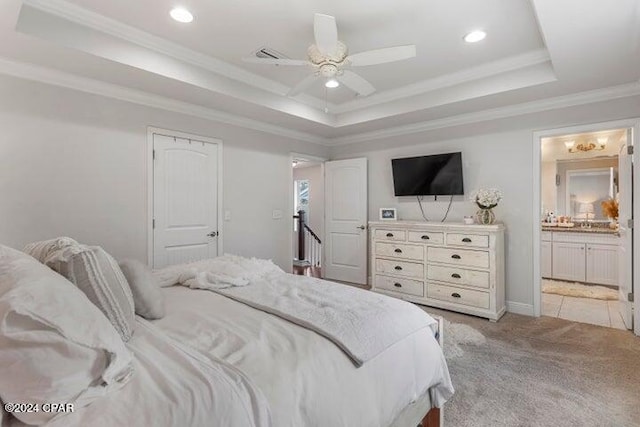 carpeted bedroom with a tray ceiling, ceiling fan, ornamental molding, and ensuite bath