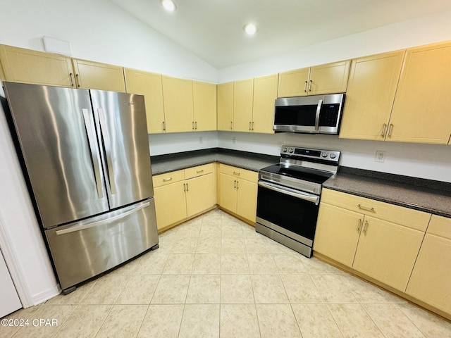 kitchen with vaulted ceiling, stainless steel appliances, dark countertops, and light tile patterned flooring