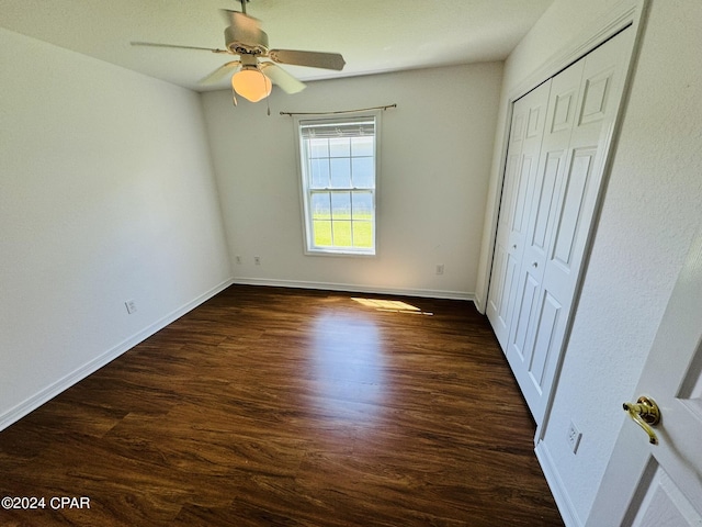 unfurnished bedroom with ceiling fan, a closet, dark wood finished floors, and baseboards