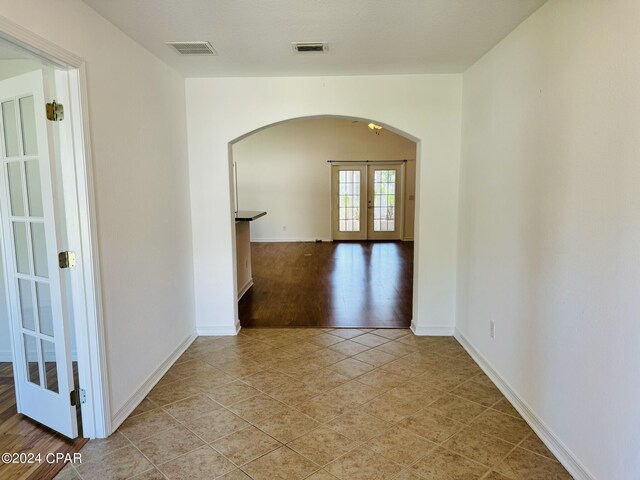 spare room featuring arched walkways, french doors, light tile patterned floors, and visible vents