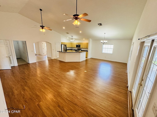 unfurnished living room featuring arched walkways, baseboards, light wood-style flooring, high vaulted ceiling, and ceiling fan with notable chandelier