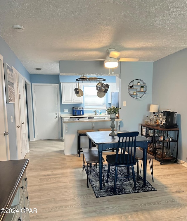 dining area featuring light wood-type flooring, ceiling fan, and a textured ceiling