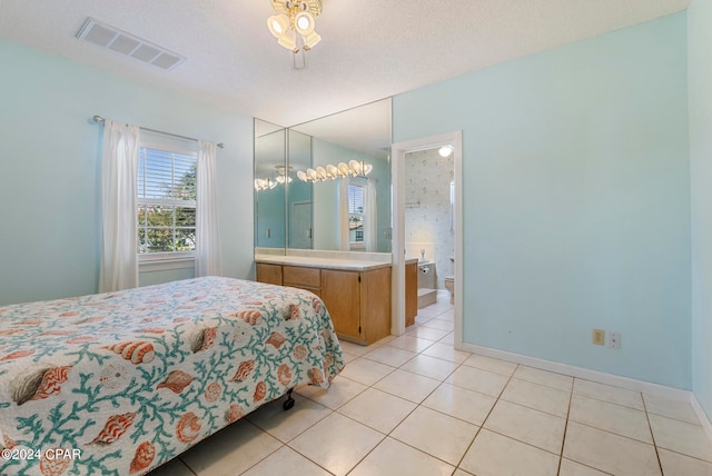 tiled bedroom with a textured ceiling, a chandelier, and ensuite bathroom