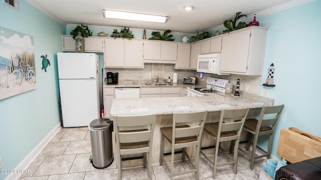 kitchen featuring white appliances, a kitchen bar, crown molding, and kitchen peninsula