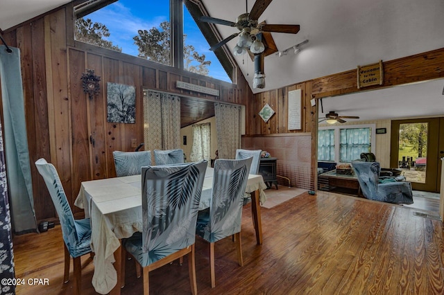 dining room featuring wooden walls, ceiling fan, high vaulted ceiling, and wood-type flooring