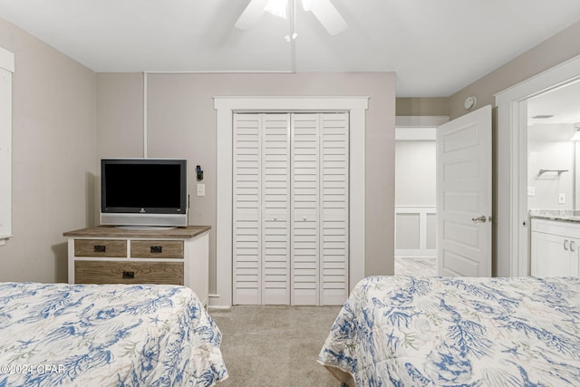 bedroom with ceiling fan, ensuite bathroom, light colored carpet, and a closet