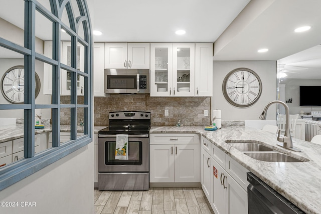 kitchen with stainless steel appliances, light stone countertops, sink, and white cabinets