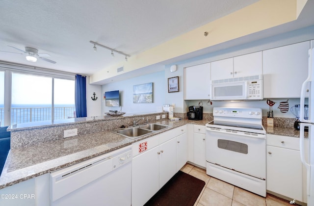 kitchen featuring white appliances, a peninsula, a textured ceiling, light tile patterned floors, and a sink