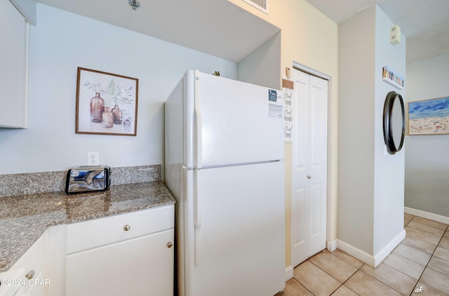 kitchen featuring baseboards, freestanding refrigerator, white cabinetry, light tile patterned flooring, and light stone counters