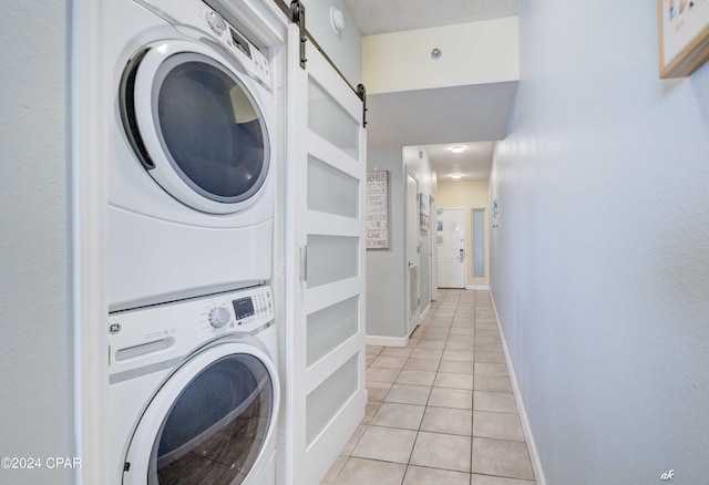 clothes washing area featuring laundry area, a barn door, light tile patterned flooring, stacked washer and clothes dryer, and baseboards