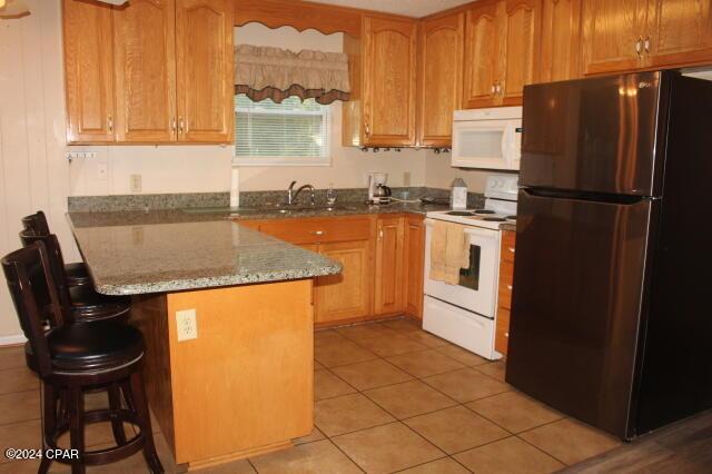 kitchen featuring sink, a breakfast bar area, light tile patterned floors, stone counters, and white appliances