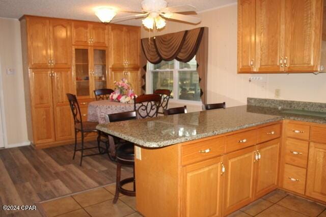 kitchen with stone counters, hardwood / wood-style floors, a breakfast bar area, ceiling fan, and kitchen peninsula