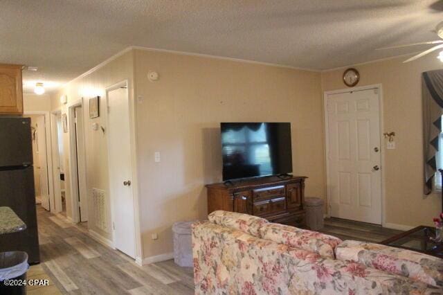 living room featuring hardwood / wood-style flooring, ceiling fan, ornamental molding, and a textured ceiling