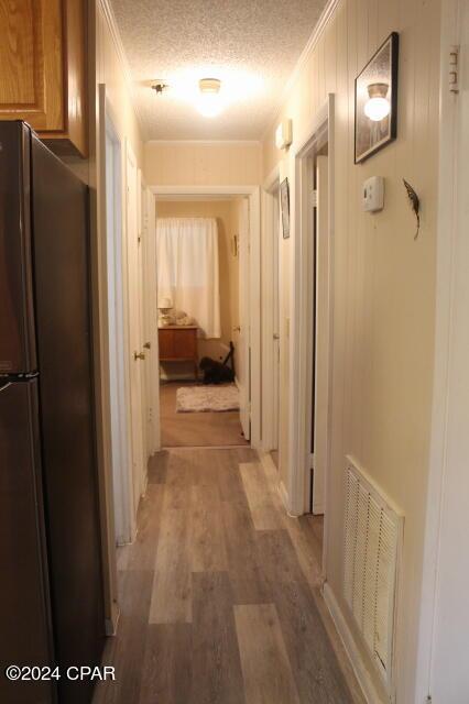 corridor featuring ornamental molding, wood-type flooring, and a textured ceiling