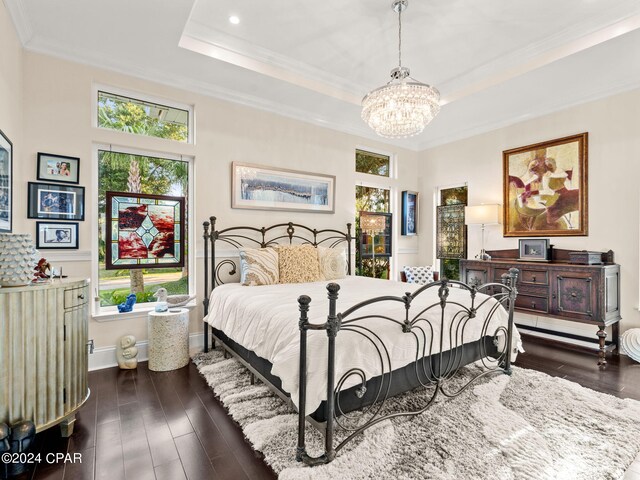 bedroom featuring dark wood-type flooring, a raised ceiling, ornamental molding, and a chandelier