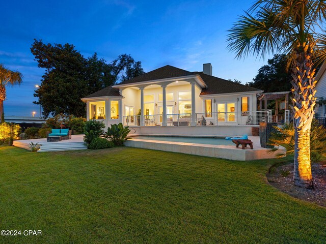 back house at dusk featuring a patio and a lawn