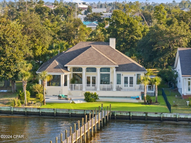 rear view of house with a patio, a balcony, a shingled roof, a water view, and a lawn