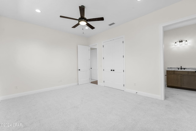 unfurnished bedroom with a closet, ceiling fan, ensuite bathroom, sink, and light colored carpet