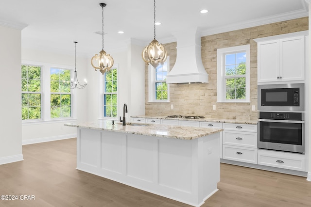 kitchen featuring appliances with stainless steel finishes, light hardwood / wood-style floors, white cabinetry, custom exhaust hood, and a center island with sink