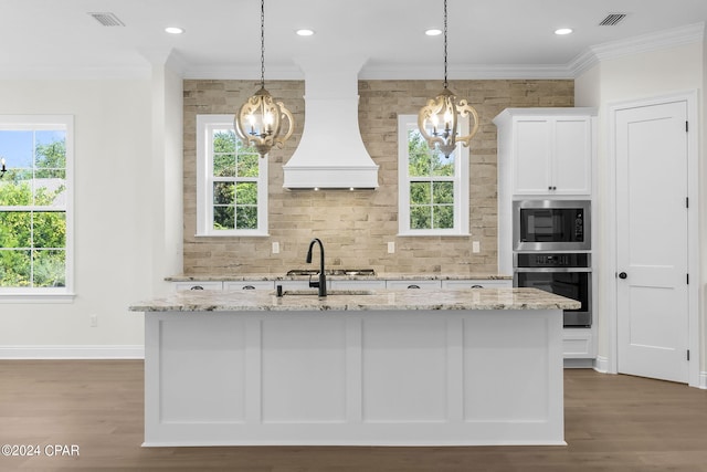 kitchen featuring a center island with sink, white cabinetry, light stone counters, and stainless steel oven