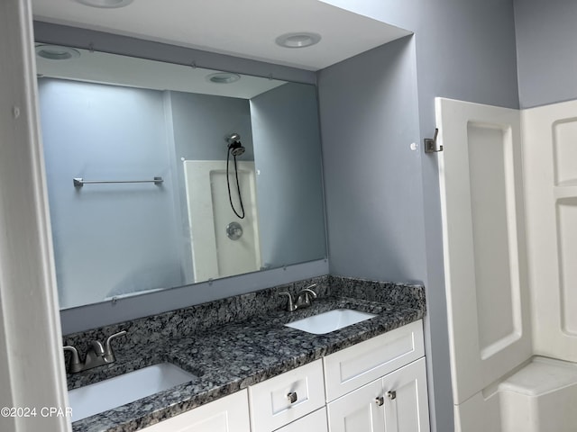 bathroom with double vanity, walk in shower, and a sink