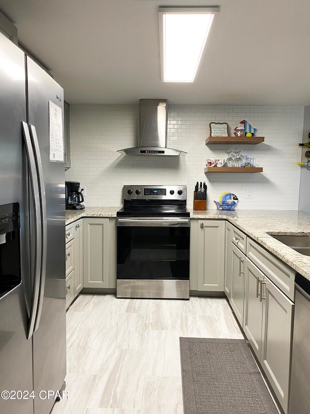 kitchen featuring stainless steel appliances, wall chimney range hood, light stone counters, and decorative backsplash