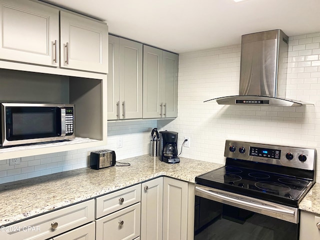 kitchen featuring appliances with stainless steel finishes, light stone countertops, wall chimney exhaust hood, gray cabinetry, and decorative backsplash