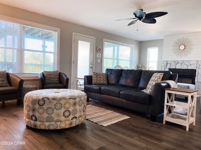 living room with ceiling fan, dark hardwood / wood-style floors, and a stone fireplace