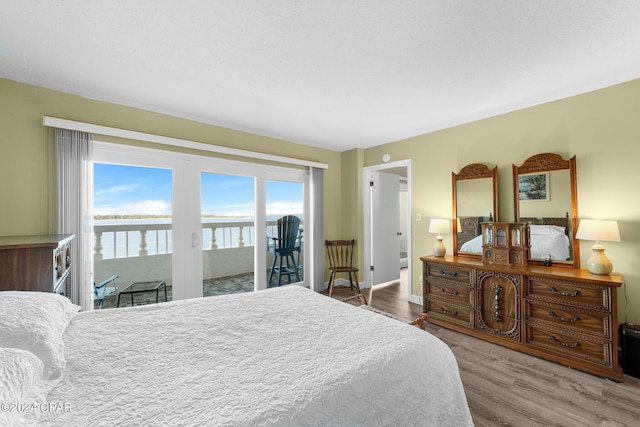 bedroom with baseboards, a water view, wood finished floors, and access to exterior