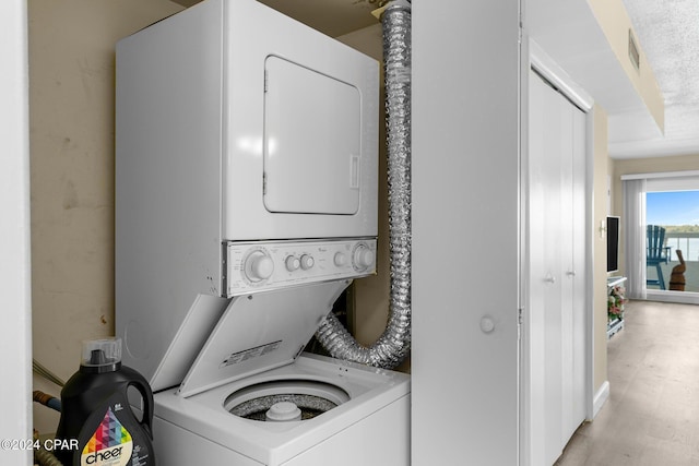 clothes washing area with visible vents, light wood finished floors, and stacked washing maching and dryer