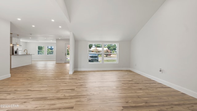 unfurnished living room with light hardwood / wood-style floors, vaulted ceiling, and plenty of natural light