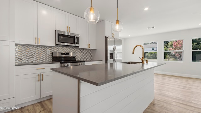 kitchen featuring a center island with sink, appliances with stainless steel finishes, hanging light fixtures, and sink