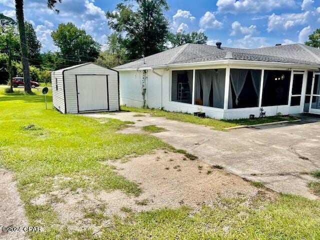 rear view of property featuring a sunroom, a lawn, and a shed