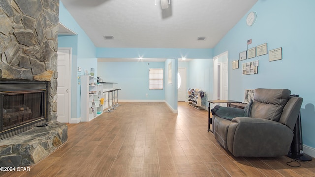 living area featuring vaulted ceiling, light hardwood / wood-style floors, and a stone fireplace