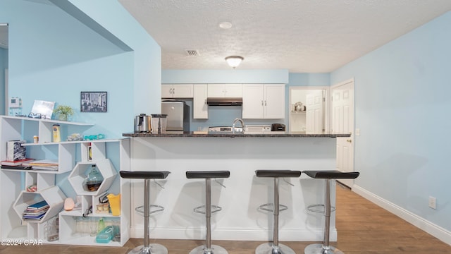 kitchen with dark stone counters, a textured ceiling, light hardwood / wood-style floors, white cabinetry, and stainless steel fridge