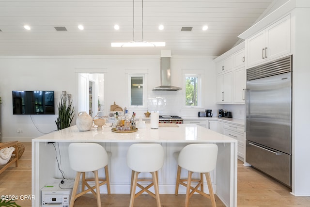 kitchen featuring backsplash, light hardwood / wood-style flooring, built in refrigerator, a center island with sink, and wall chimney range hood