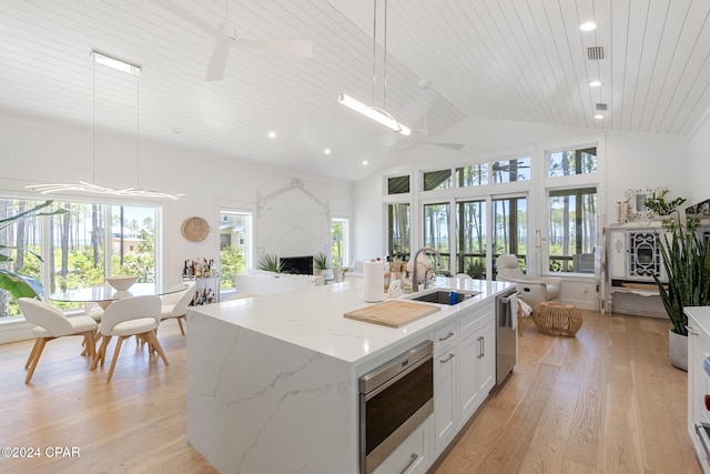 kitchen featuring a wealth of natural light, decorative light fixtures, an island with sink, and light hardwood / wood-style flooring