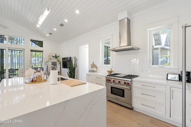 kitchen featuring decorative backsplash, wall chimney exhaust hood, light stone counters, light wood-type flooring, and premium range