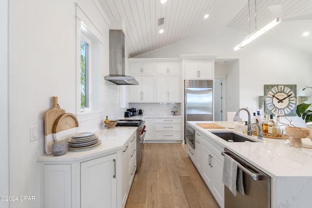 kitchen featuring wall chimney range hood, built in appliances, light hardwood / wood-style floors, sink, and lofted ceiling