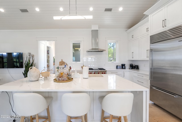 kitchen with a center island, wall chimney exhaust hood, light stone countertops, tasteful backsplash, and built in fridge