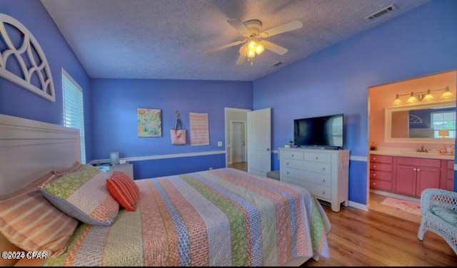 bedroom featuring light wood-type flooring, a textured ceiling, ceiling fan, lofted ceiling, and ensuite bathroom