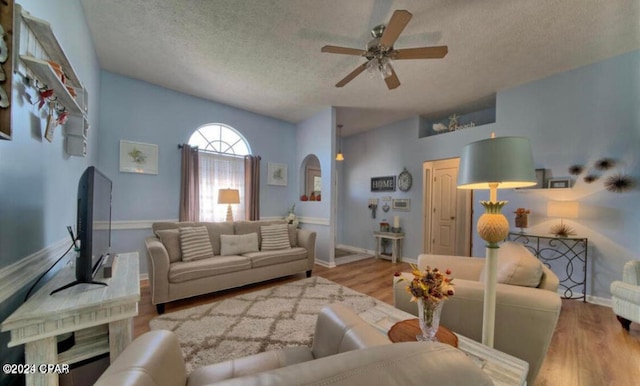 living room with a textured ceiling, ceiling fan, and light wood-type flooring