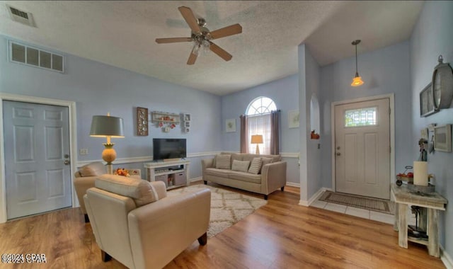 living room with a textured ceiling, ceiling fan, and light wood-type flooring