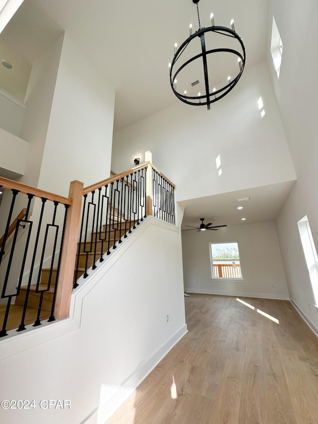 stairs featuring hardwood / wood-style flooring, ceiling fan with notable chandelier, and a high ceiling