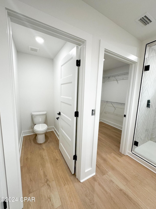 bathroom with toilet, hardwood / wood-style floors, and a shower with door