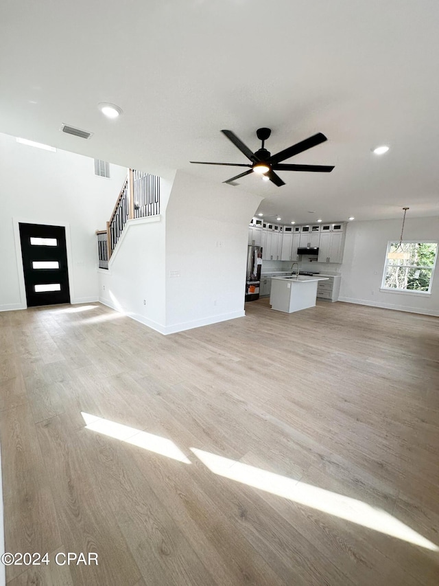 unfurnished living room featuring sink, ceiling fan with notable chandelier, and light hardwood / wood-style floors