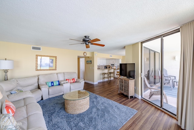 living room with baseboards, visible vents, dark wood-style floors, a wall of windows, and a textured ceiling